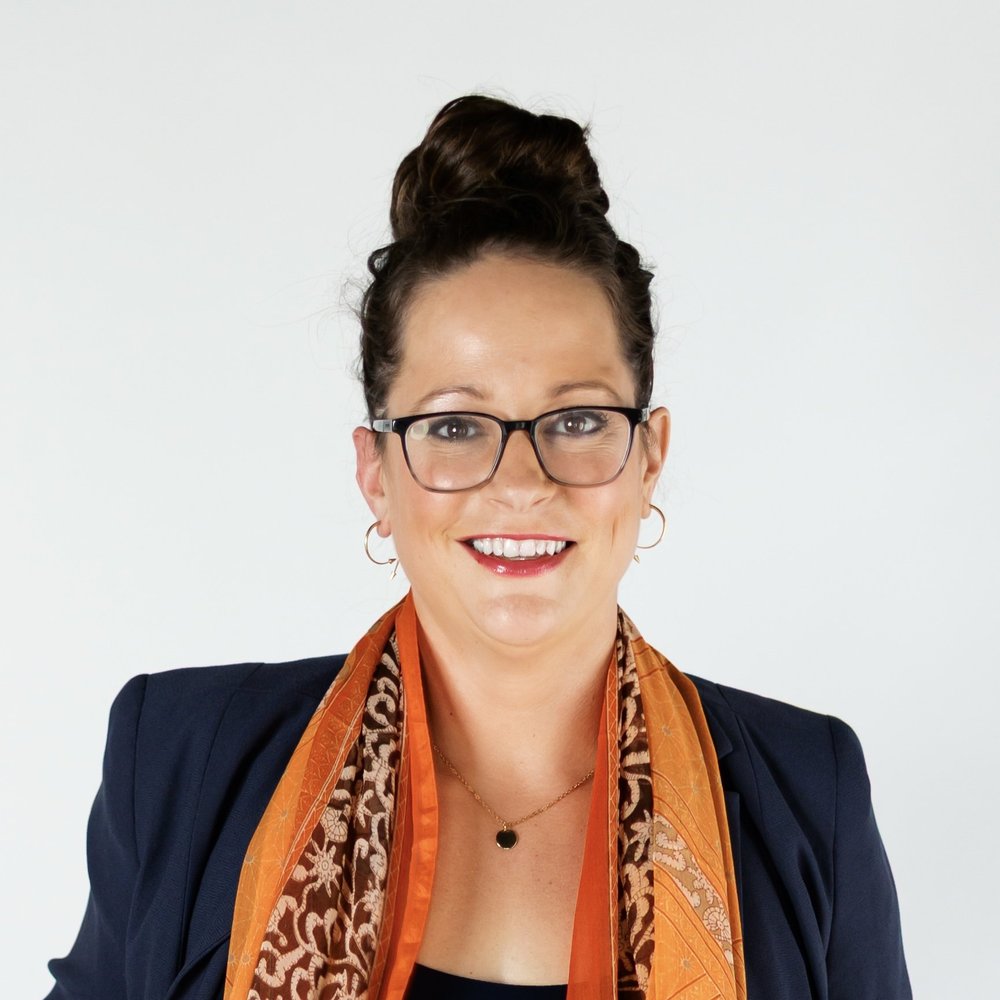 Maggie Seymour smiling in a dark blazer and orange scarf.