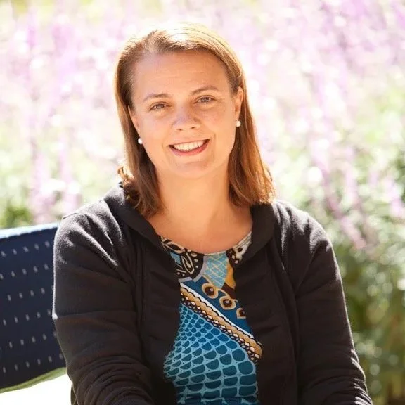 Arabella Meyer smiling outdoors with flowers and greenery in the background.