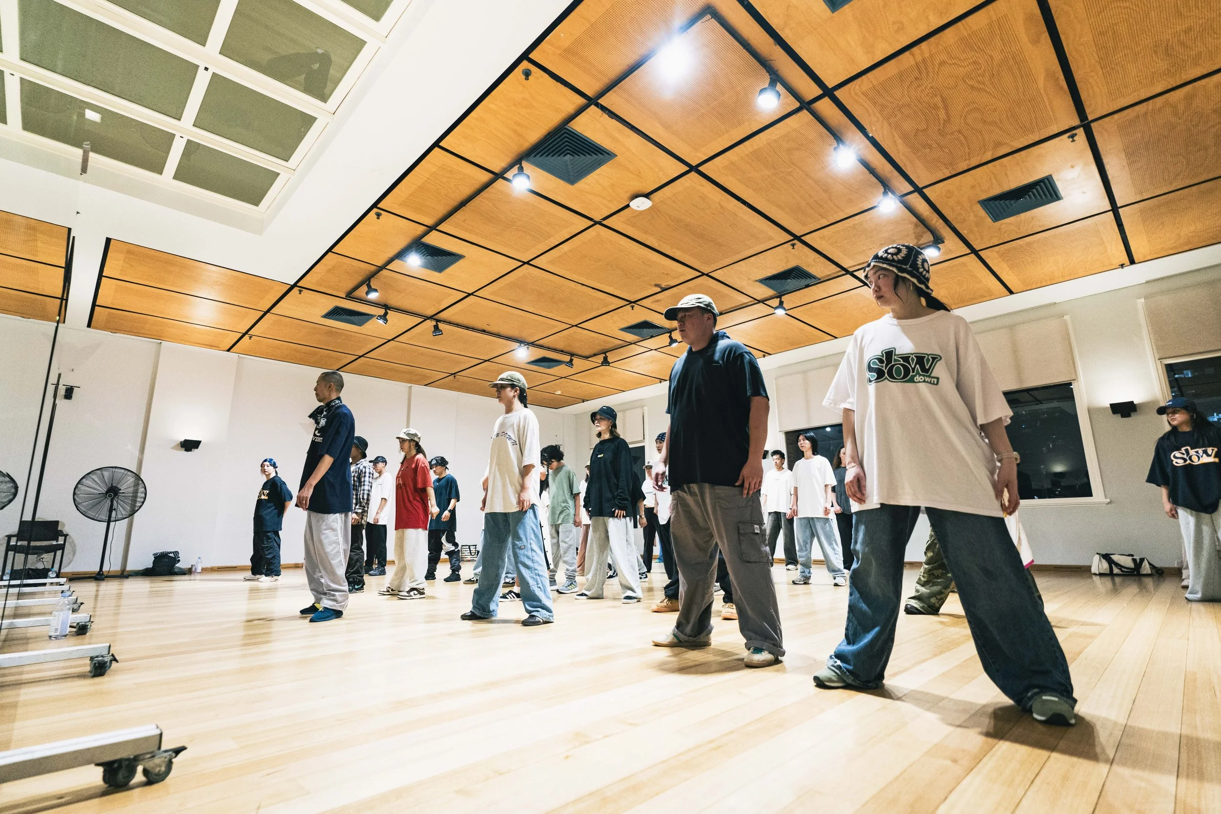 Group of people practicing dance or exercise in a dance studio with wooden floors and a ceiling with wooden panels. It's a Hip Hop class in a Perth studio.