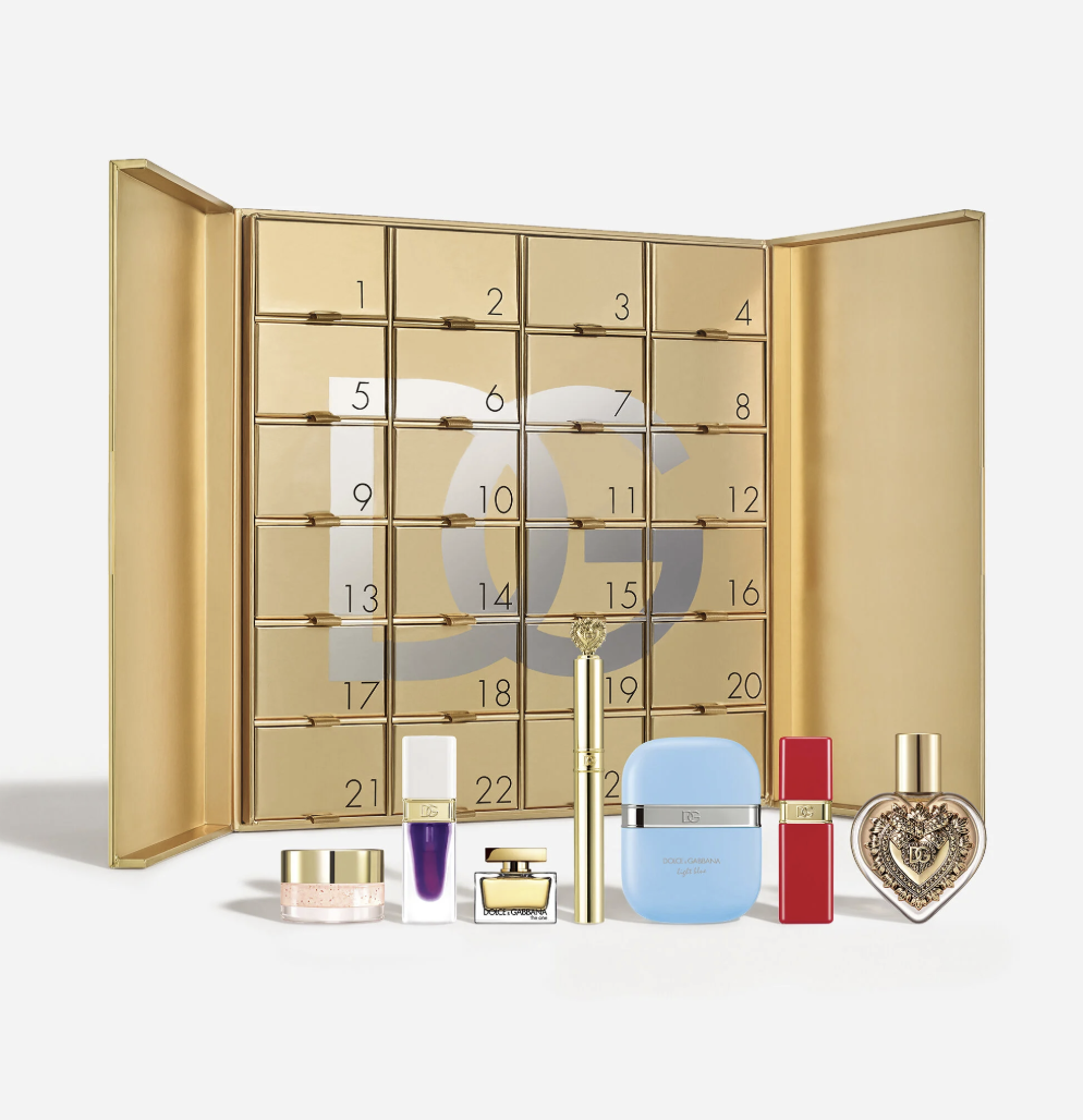 A luxurious Advent calendar with gold compartments numbered 1 to 24, accompanied by an array of high-end perfume bottles and beauty products in front.