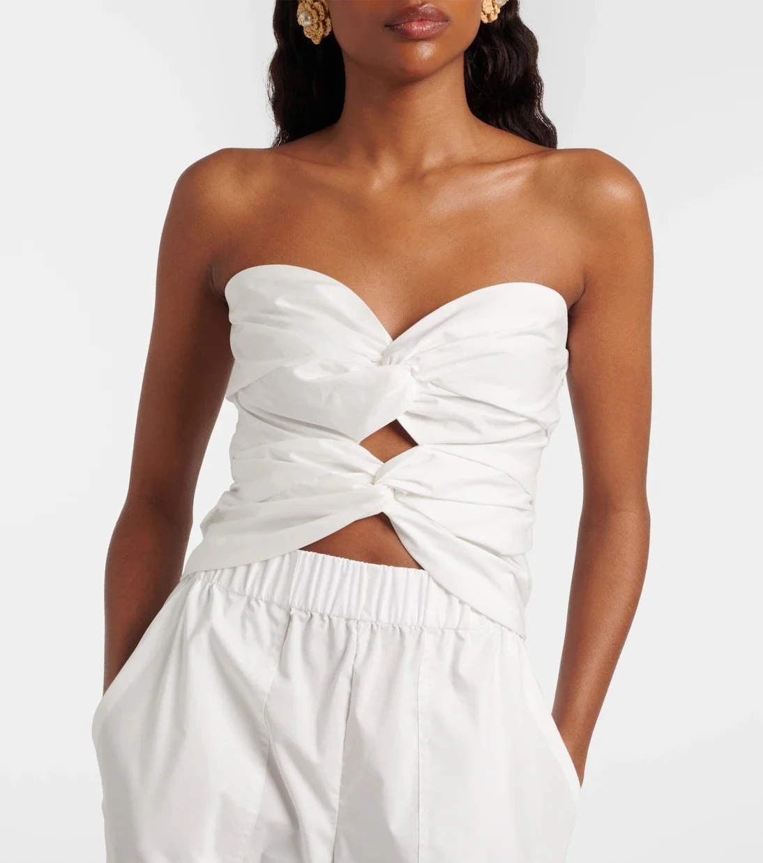 Woman wearing a white strapless top with knot details and matching white pants, standing against a plain background.