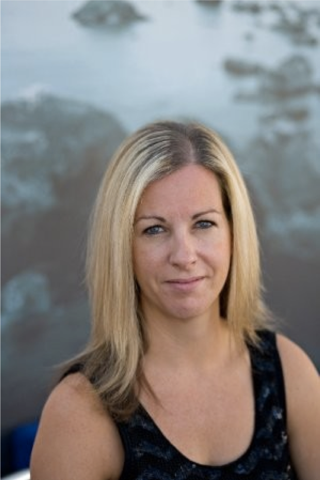 A blonde woman with straight hair wearing a black sleeveless top, standing outdoors near water.