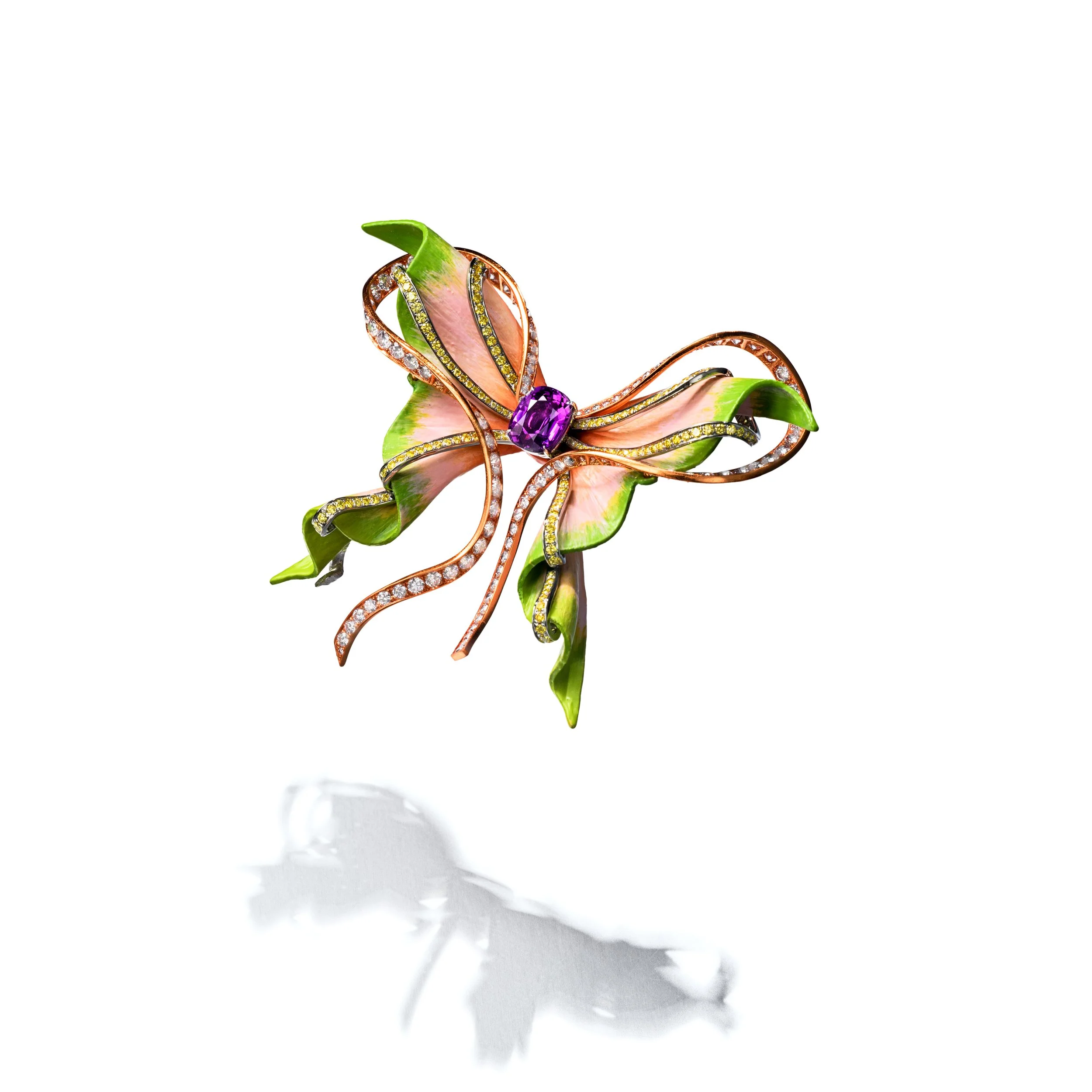 A colorful butterfly-shaped brooch with pink, green, and gold accents, decorated with small gemstones, resting on a white surface.