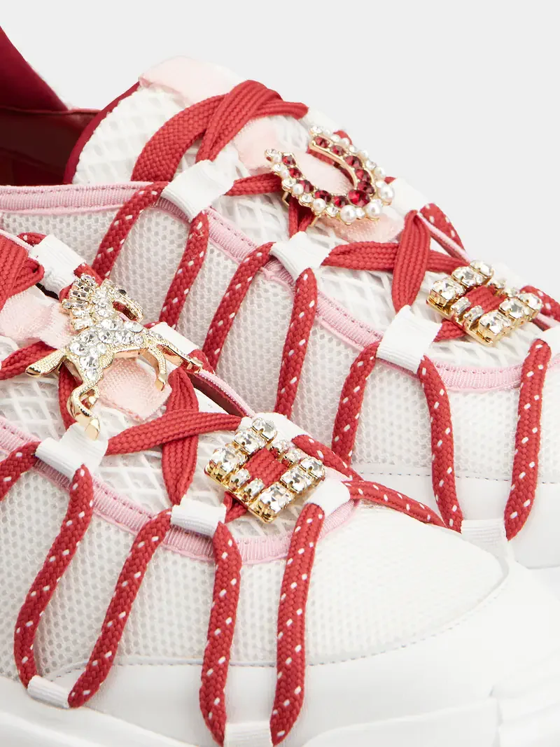 Close-up of white sneakers with red laces and decorative rhinestone charms, including a butterfly and a crescent moon with pearls.