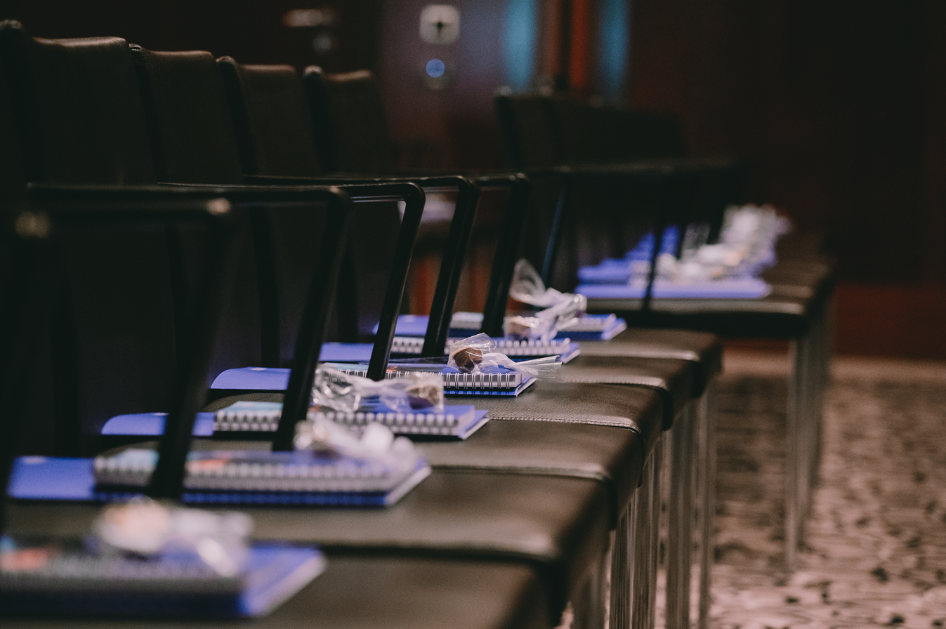 Sitzreihen in einem Auditorium mit Notizblöcken, Stiften und kleinen Verpackungen auf den Stühlen.