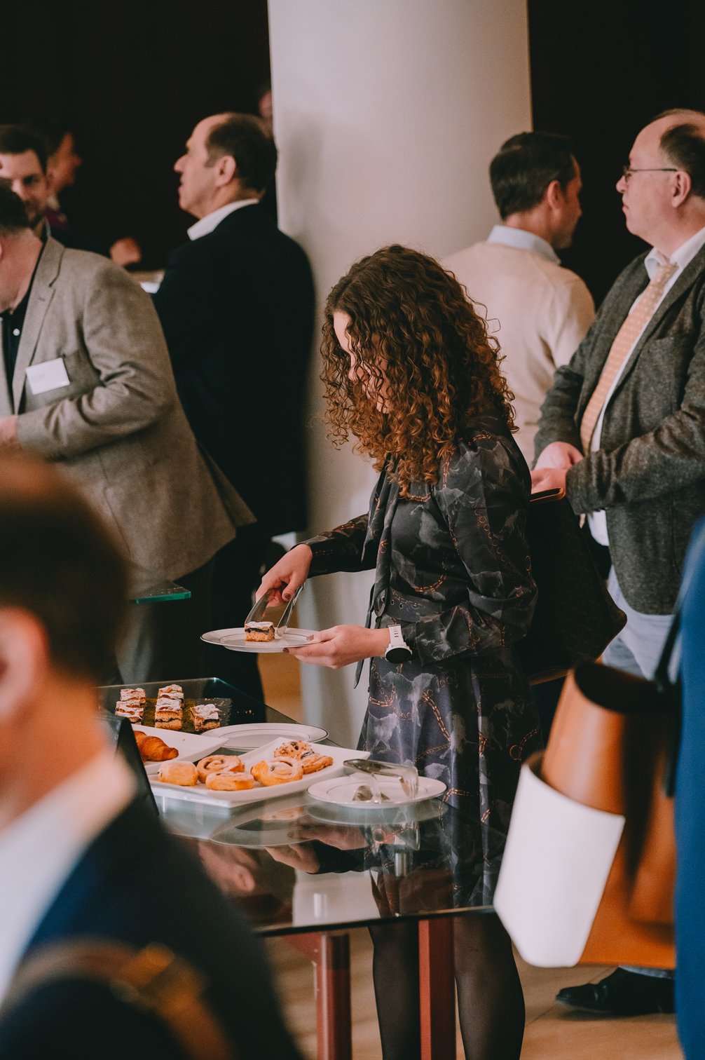 Eine Frau mit lockigem Haar bedient sich an einem Buffet mit verschiedenen Gebäckstücken bei einer Veranstaltung.