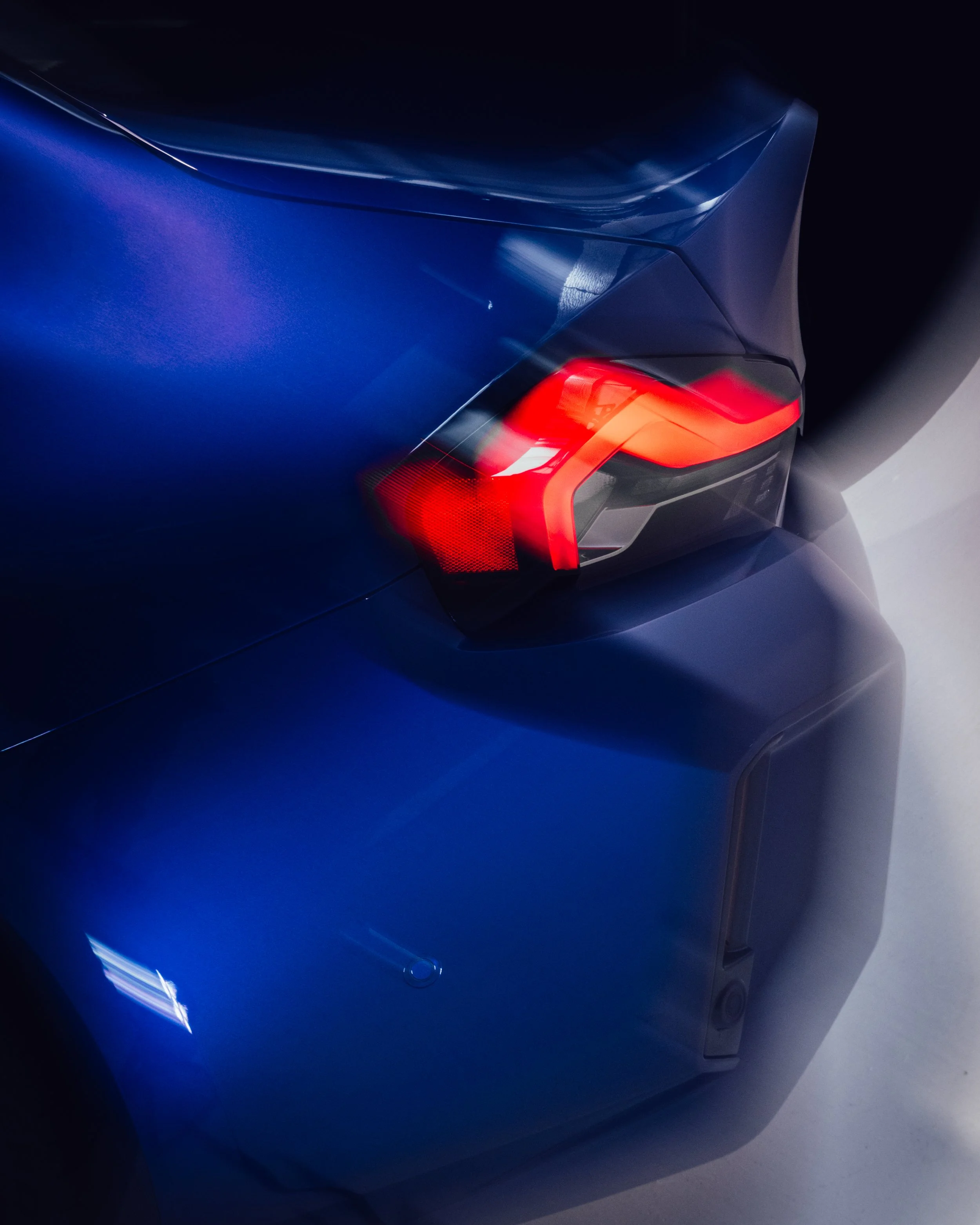 Nahaufnahme des hinteren Teils eines blauen Autos mit glänzender Oberfläche und rotem Rücklicht.