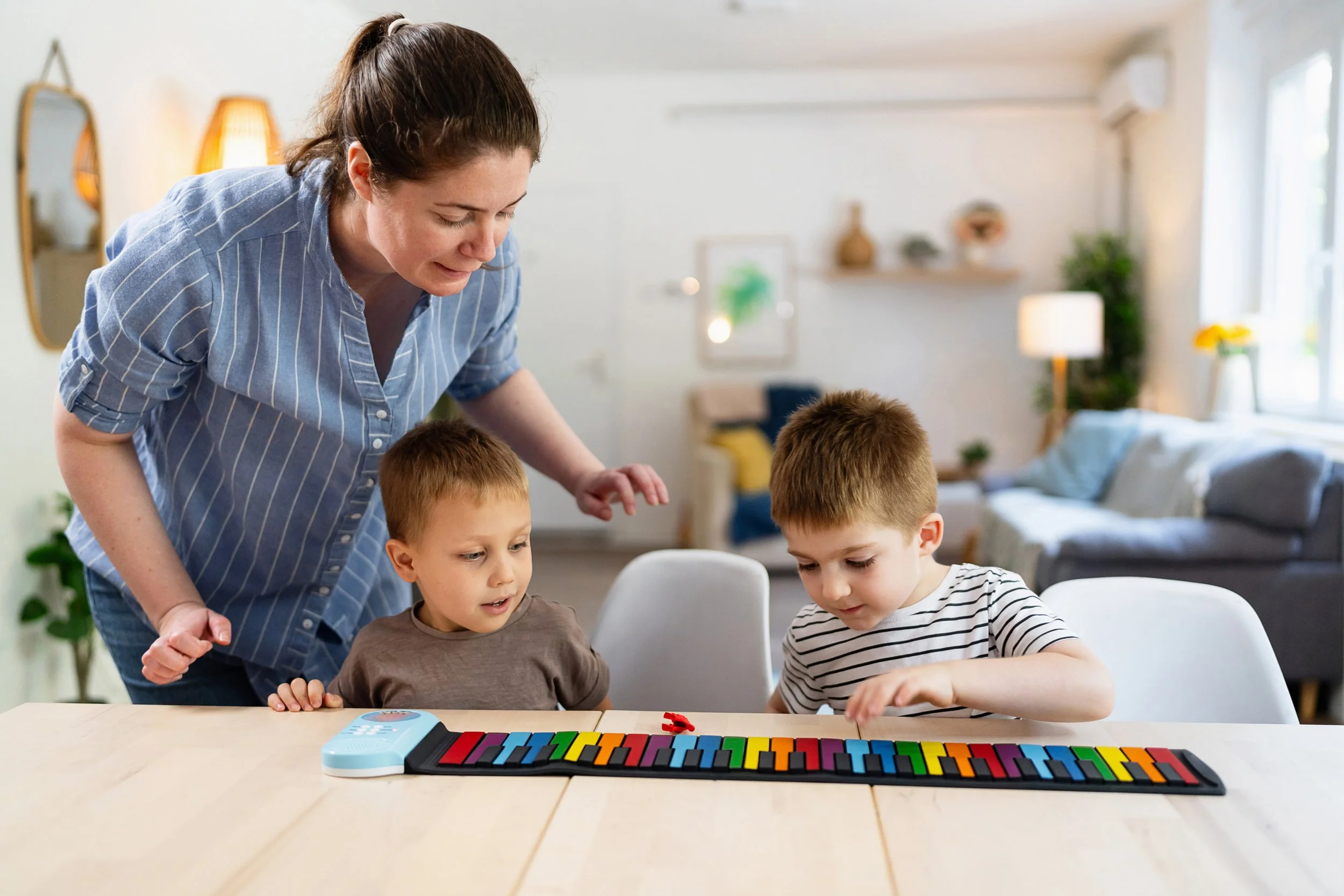 A woman looking down at twins playing a keyboard.