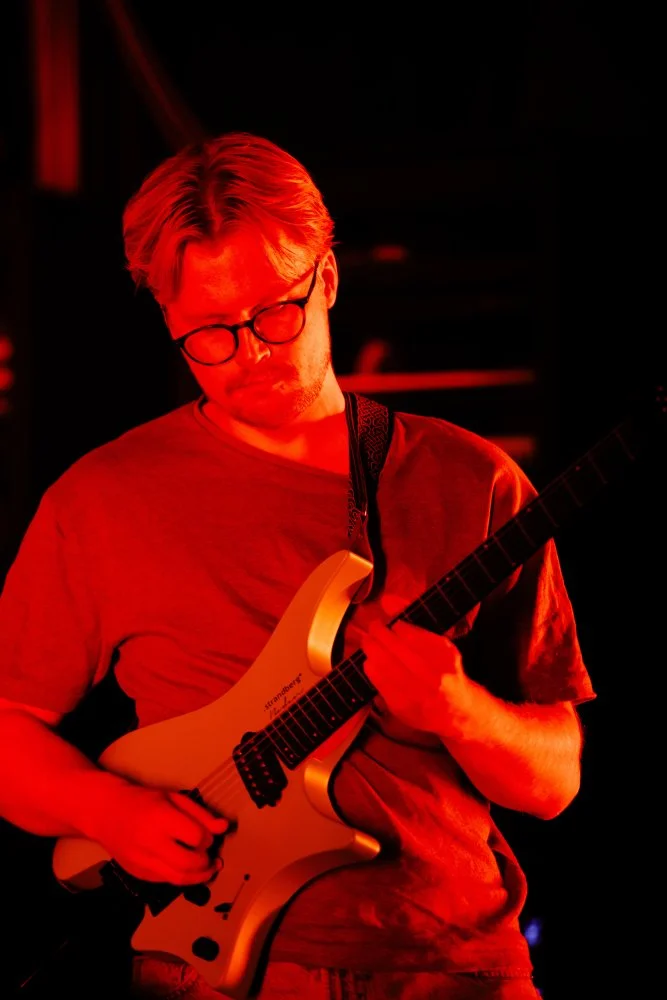 Nærbilde av en gitarist som spiller i rødt scenelys.