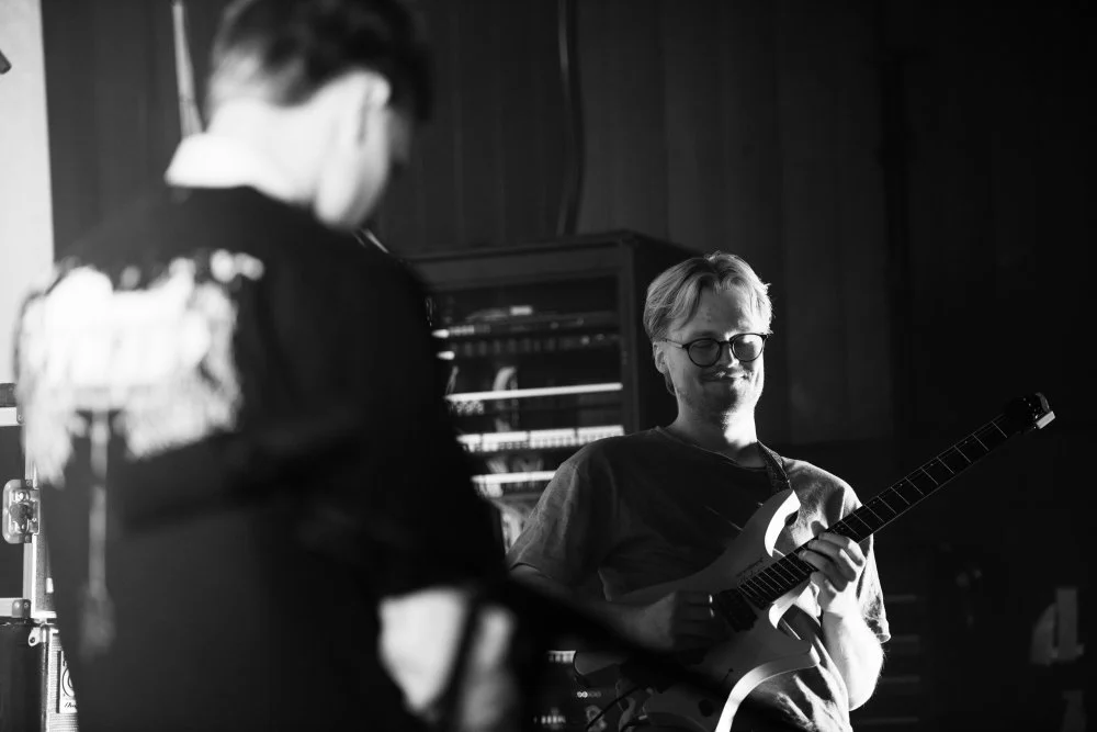 To personer med gitar og lydutstyr i et musikkrom.