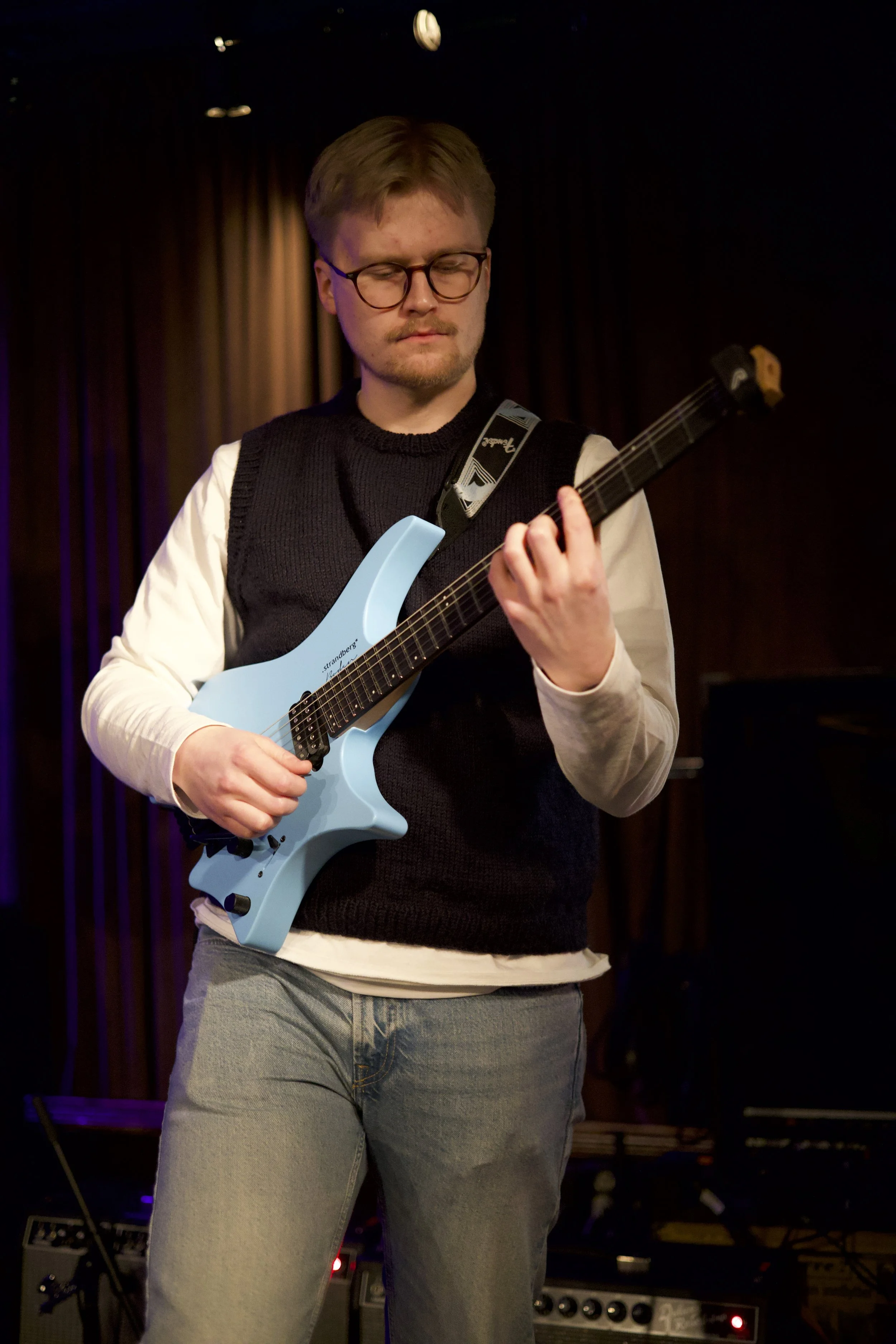 Gitarist med briller, vest og lys skjorte spiller på scenen.