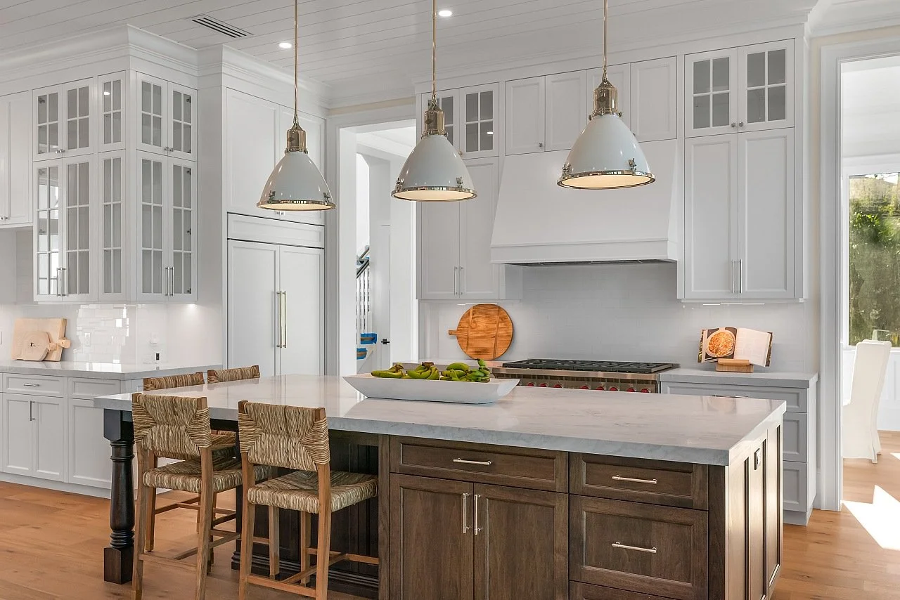 Modern white kitchen with a central island, pendant lights, and wooden barstools.