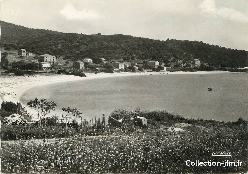 Vue en noir et blanc d'une baie avec une plage et des maisons au bord de l'eau, entourée de collines verdoyantes.