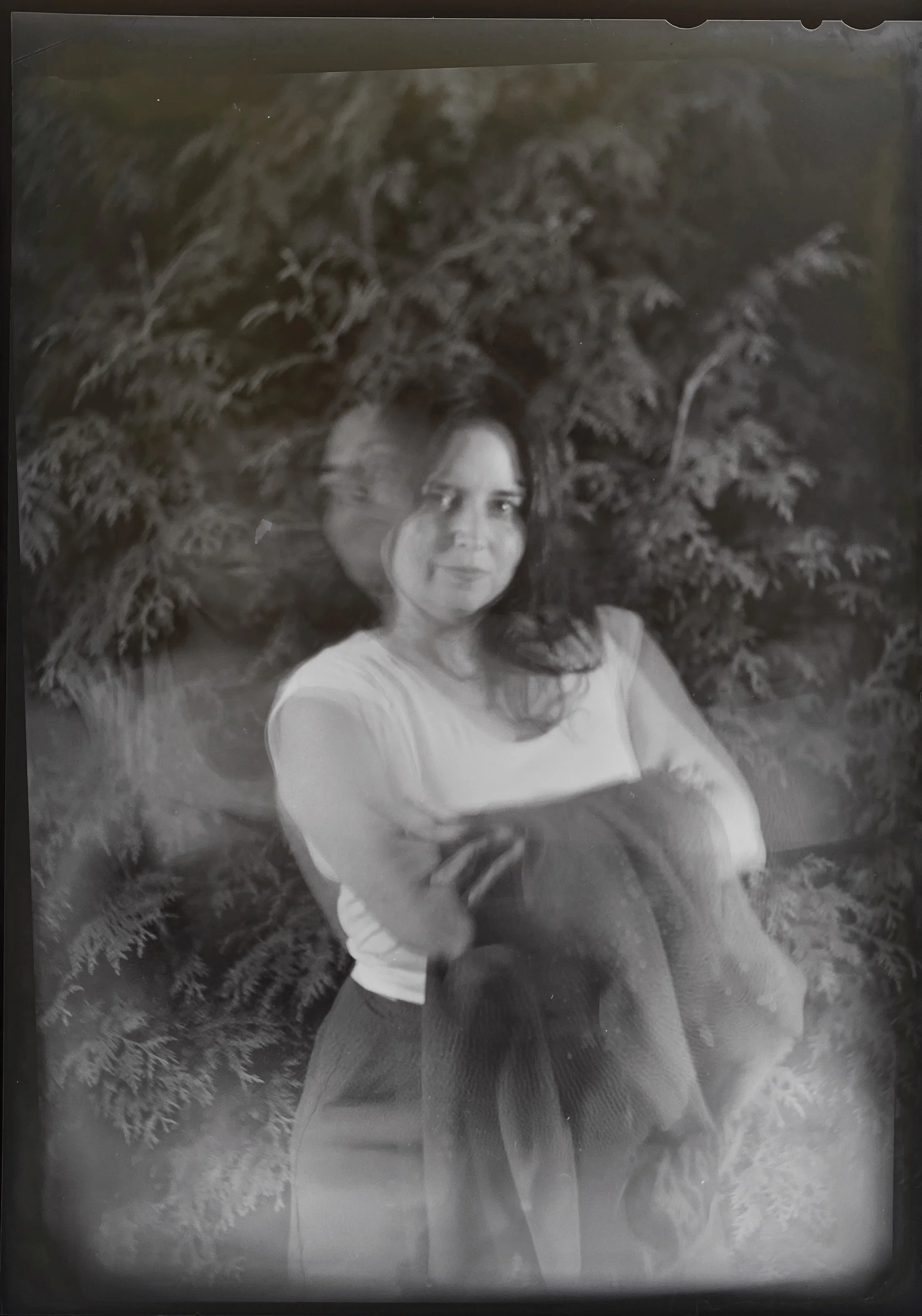 An enigmatic double exposure of Chelsea outside in front of green giants holding her jacket on hot night throwing her hair around. Made while testing the bellows of one of her view cameras for light leaks.