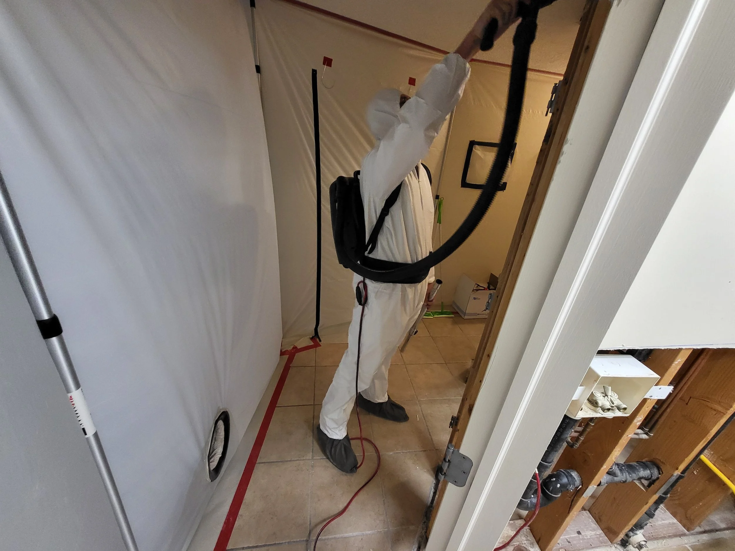 Mold remediation technician in protective equipment working inside a containment area.