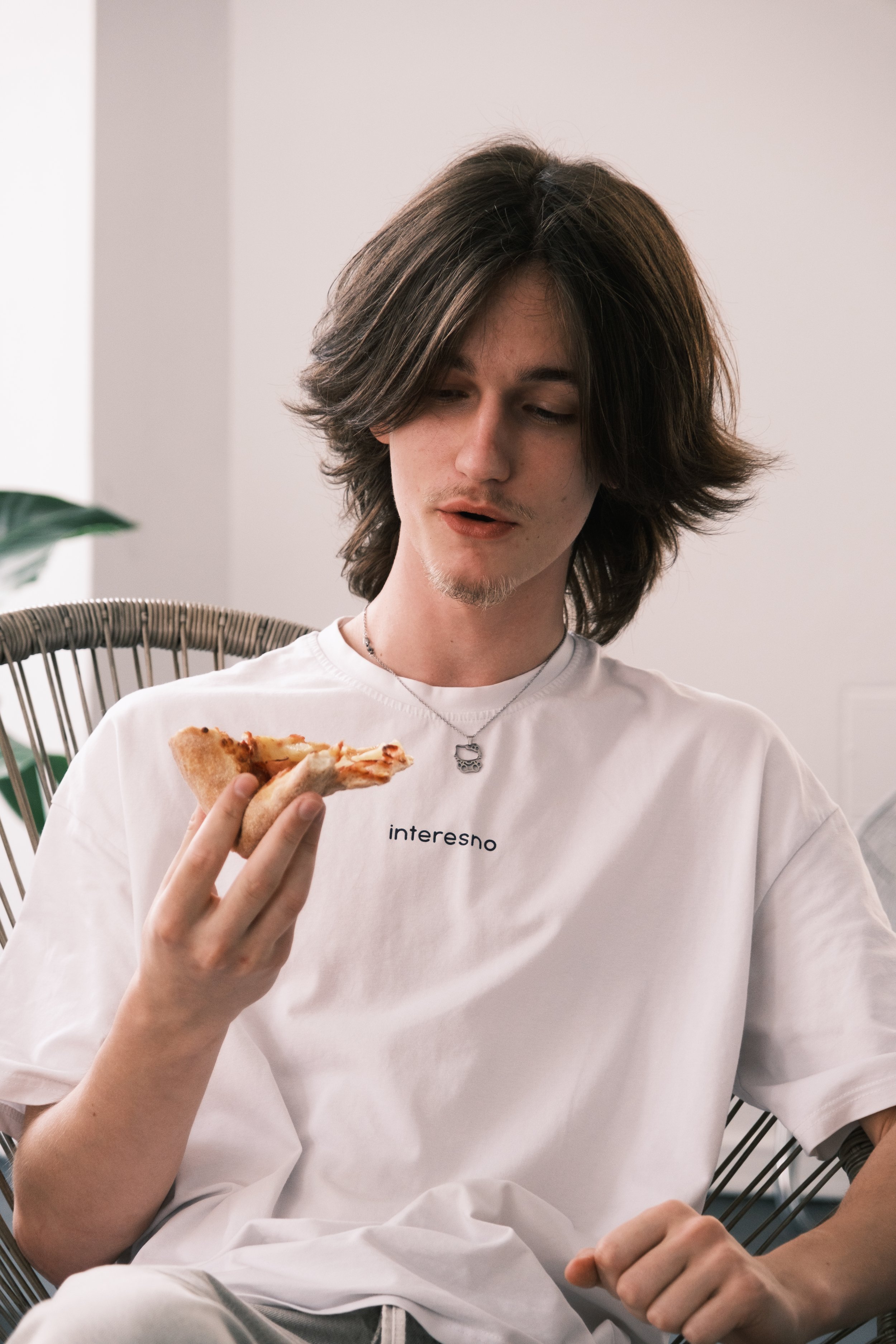 Young person in a white shirt holding a slice of pizza indoors