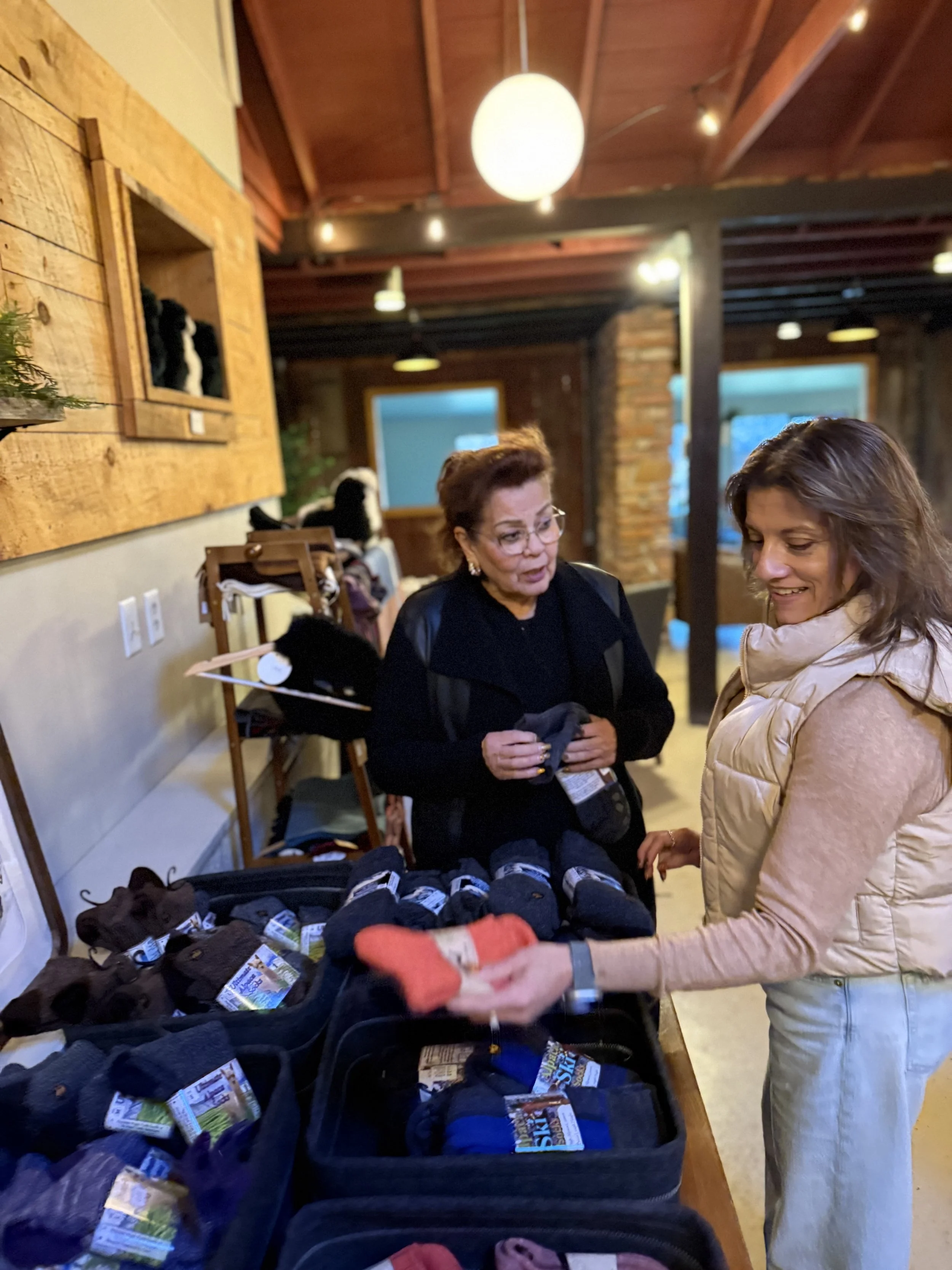 Interior view of a boutique store with clothing, accessories, and home decor items on display, wooden ceiling with hanging lights.