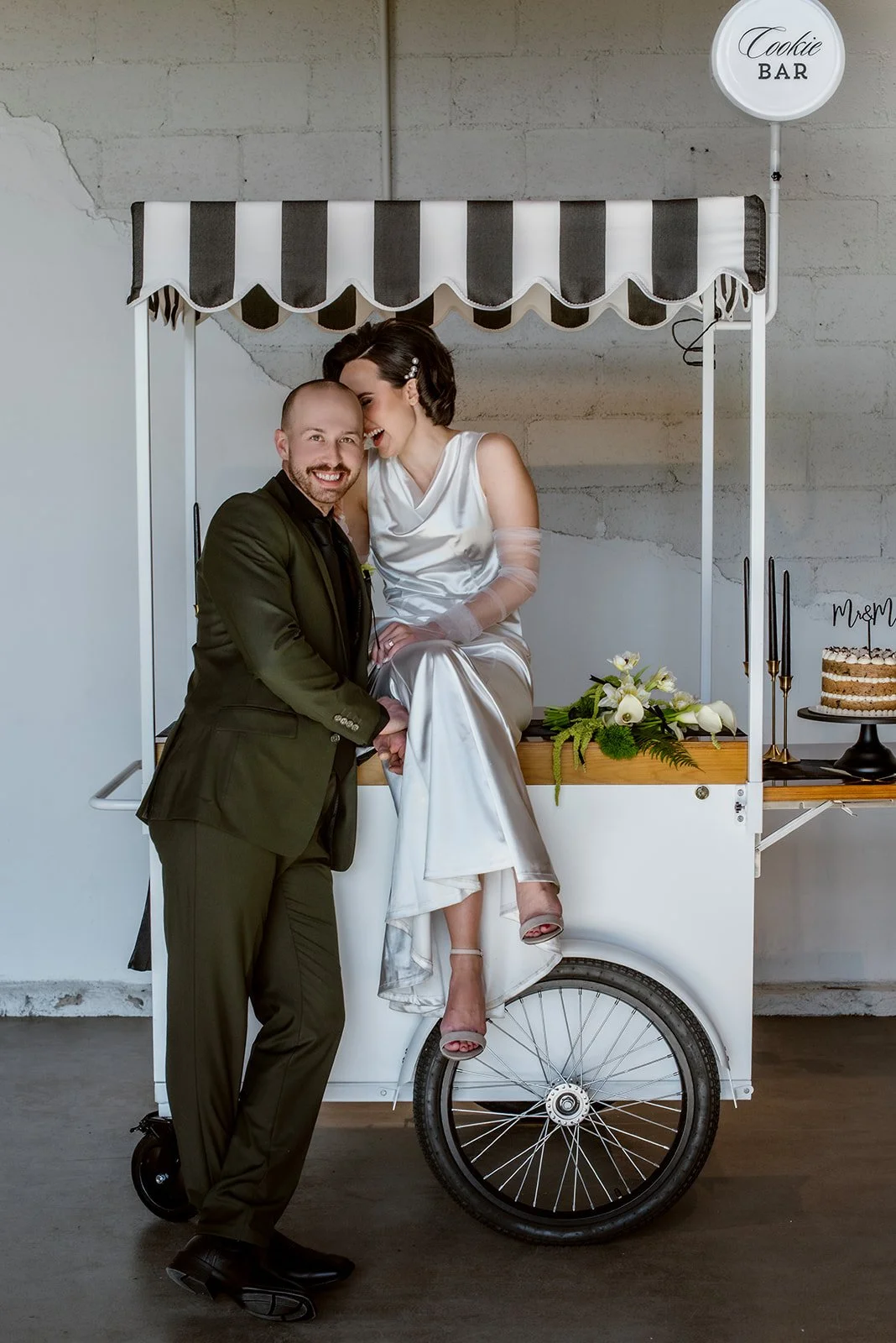 Bride seated on cookie cart with groom smiling