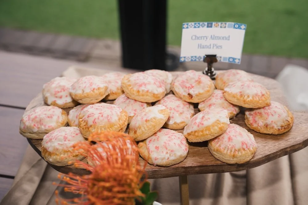 Cherry Almond Hand Pies with almond glaze and pink sugar on wooden stand, The Tiny Cookie Trolley elevated nostalgic dessert catering Denver