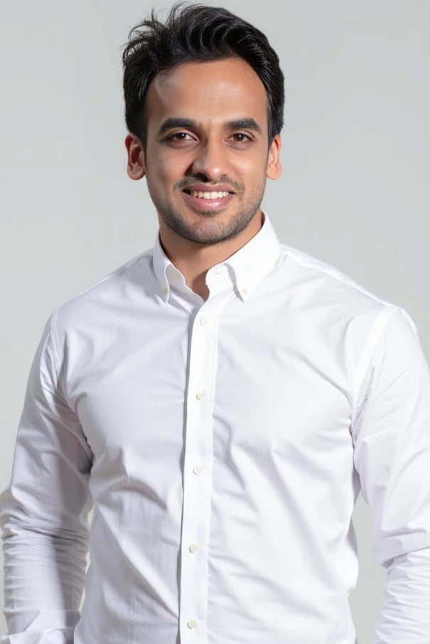 A man with dark hair wearing a white button-up shirt, smiling, against a light gray background.