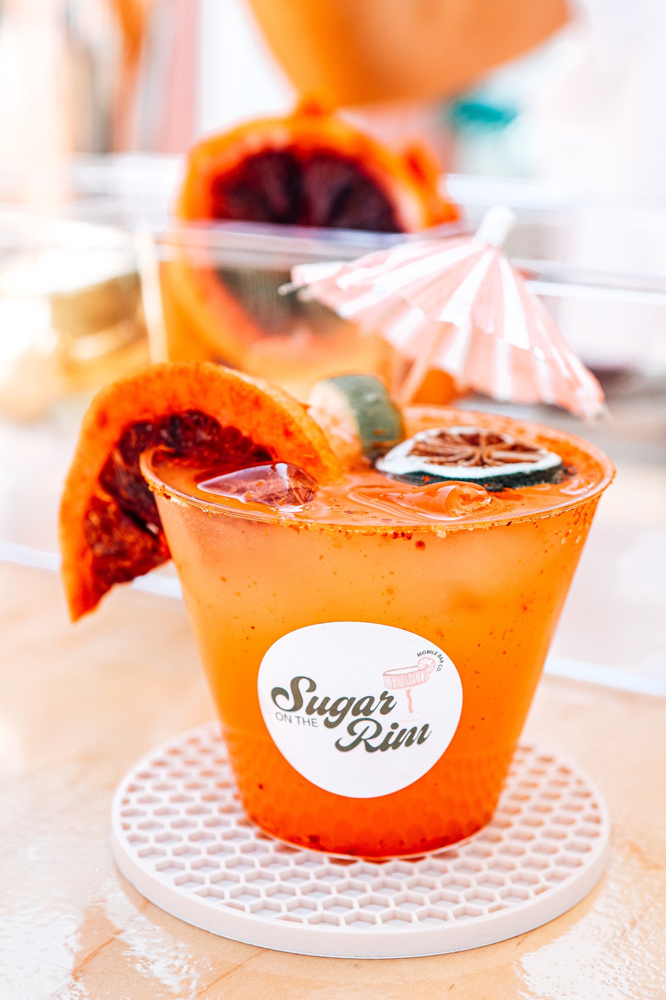 Aperol spritz drinks with orange slices and striped straws on a clear display stand, with a sign reading 'FEELING SPRITZ-Y' repeatedly.