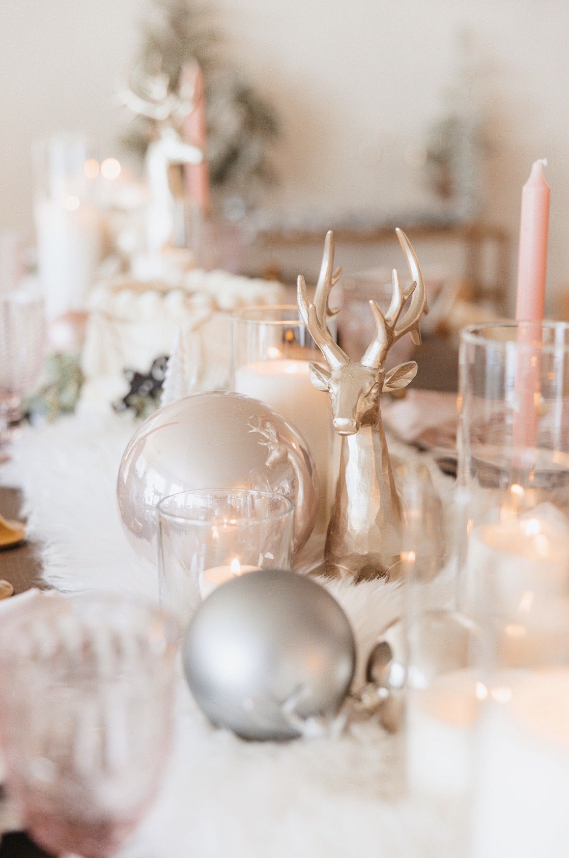 Elegant holiday table decor with gold deer statue, candles, glass ornaments, and fur table runner.