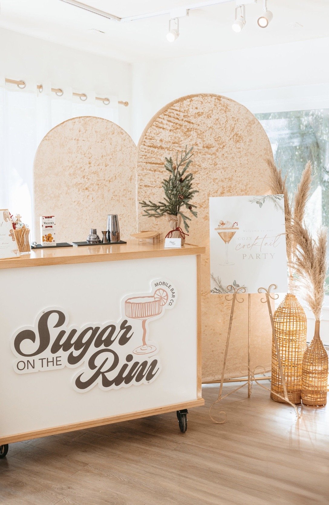 Mobile bar setup with "Sugar on the Rim" branding, featuring a countertop with drink equipment, festive decor, and a sign for a cocktail party.