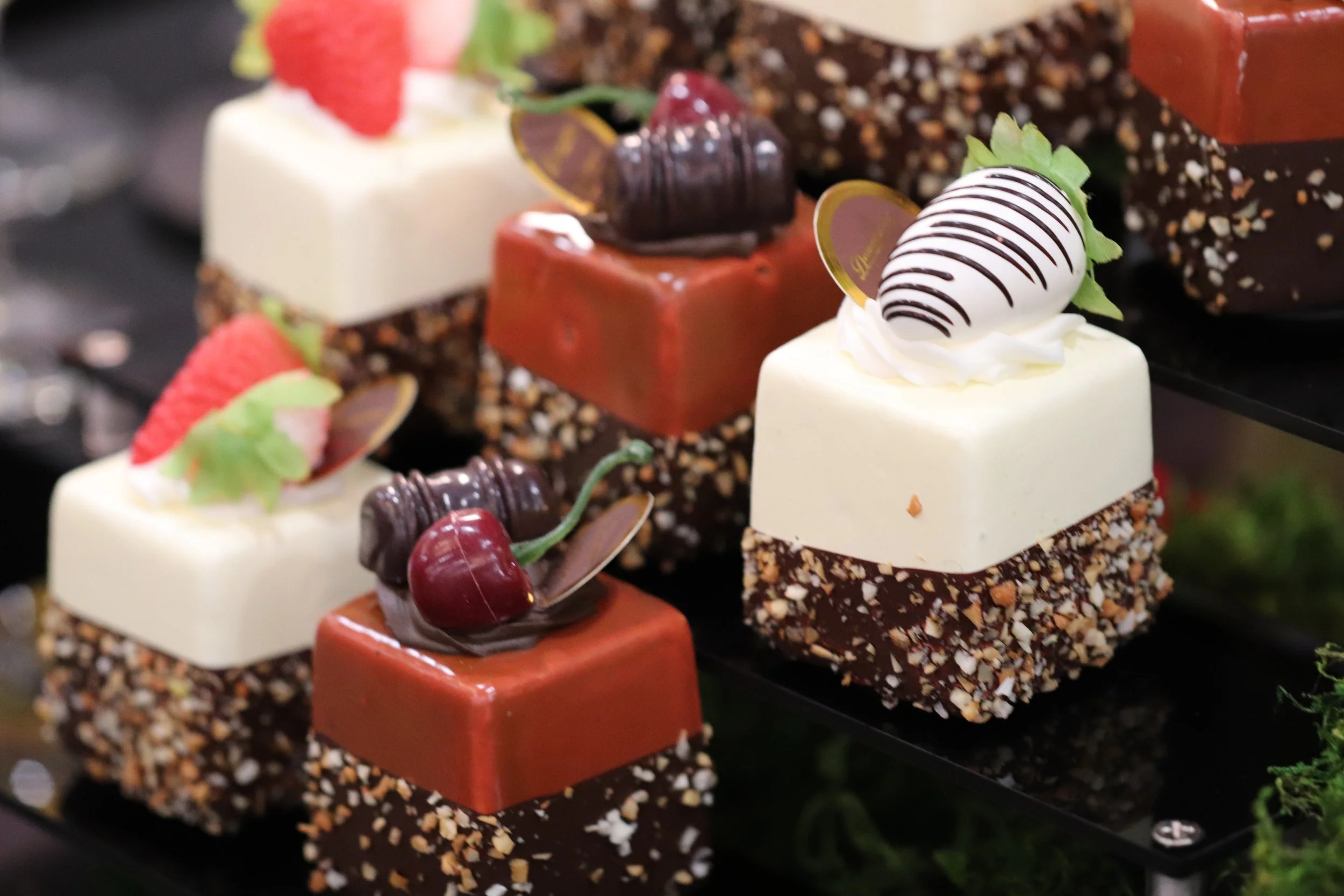 Close-up of decorated layered desserts with various chocolates, fruits, and cream, garnished with strawberries and cherries.