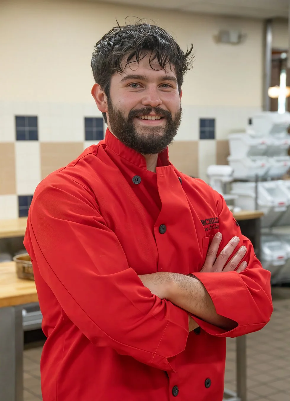 Chef Jonah Saavedra of Burchild Catering smiling in chef coat inside commercial kitchen