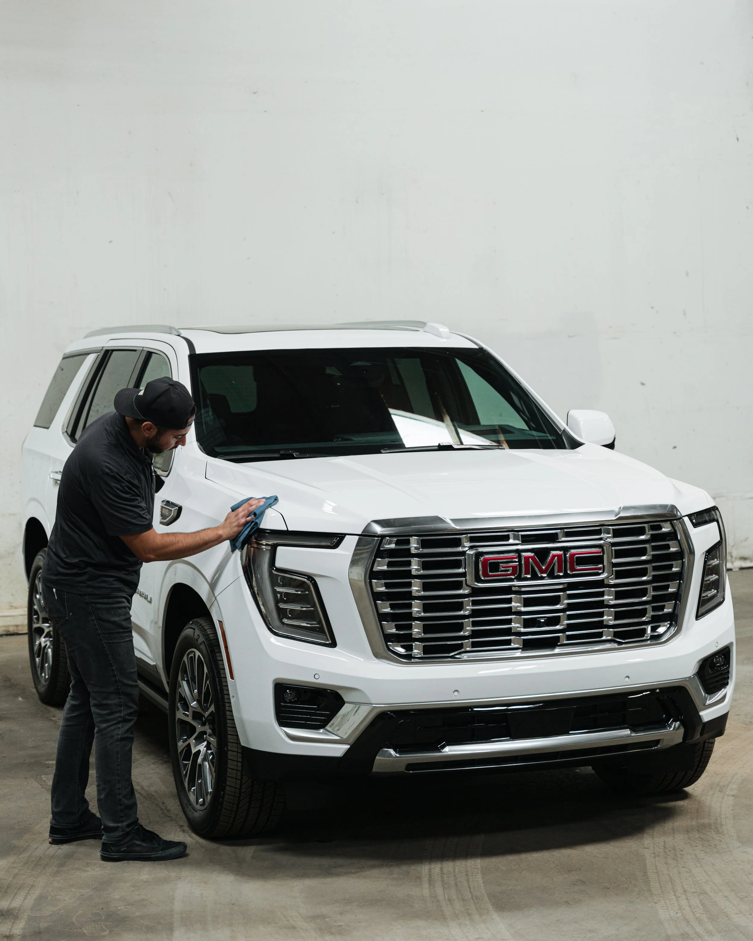 A man cleaning or inspecting a white GMC SUV inside a warehouse or garage.