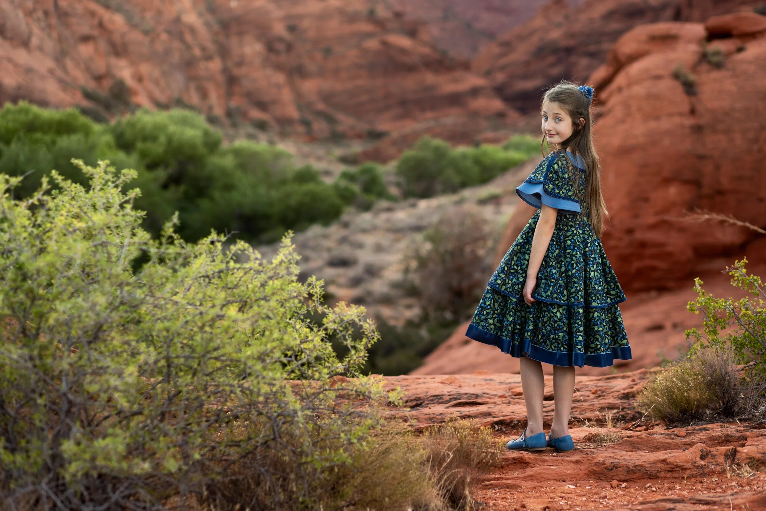 Young girl wearing a blue dress standing on the red sandstone of southern Utah over looking and epic view.