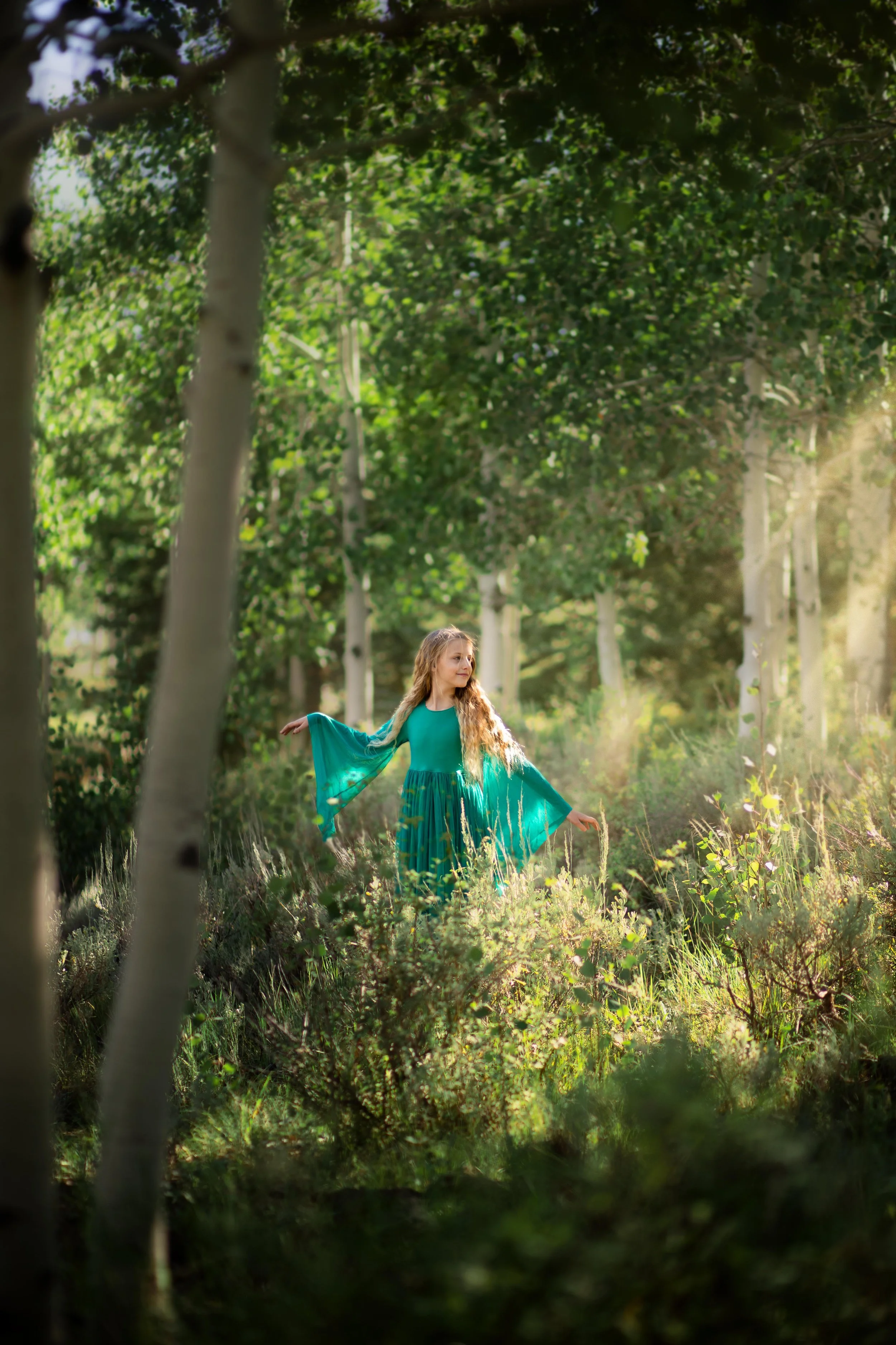 A young girl dressed as a princess wondering in an aspen forest with golden light streaks creating a magical scene.