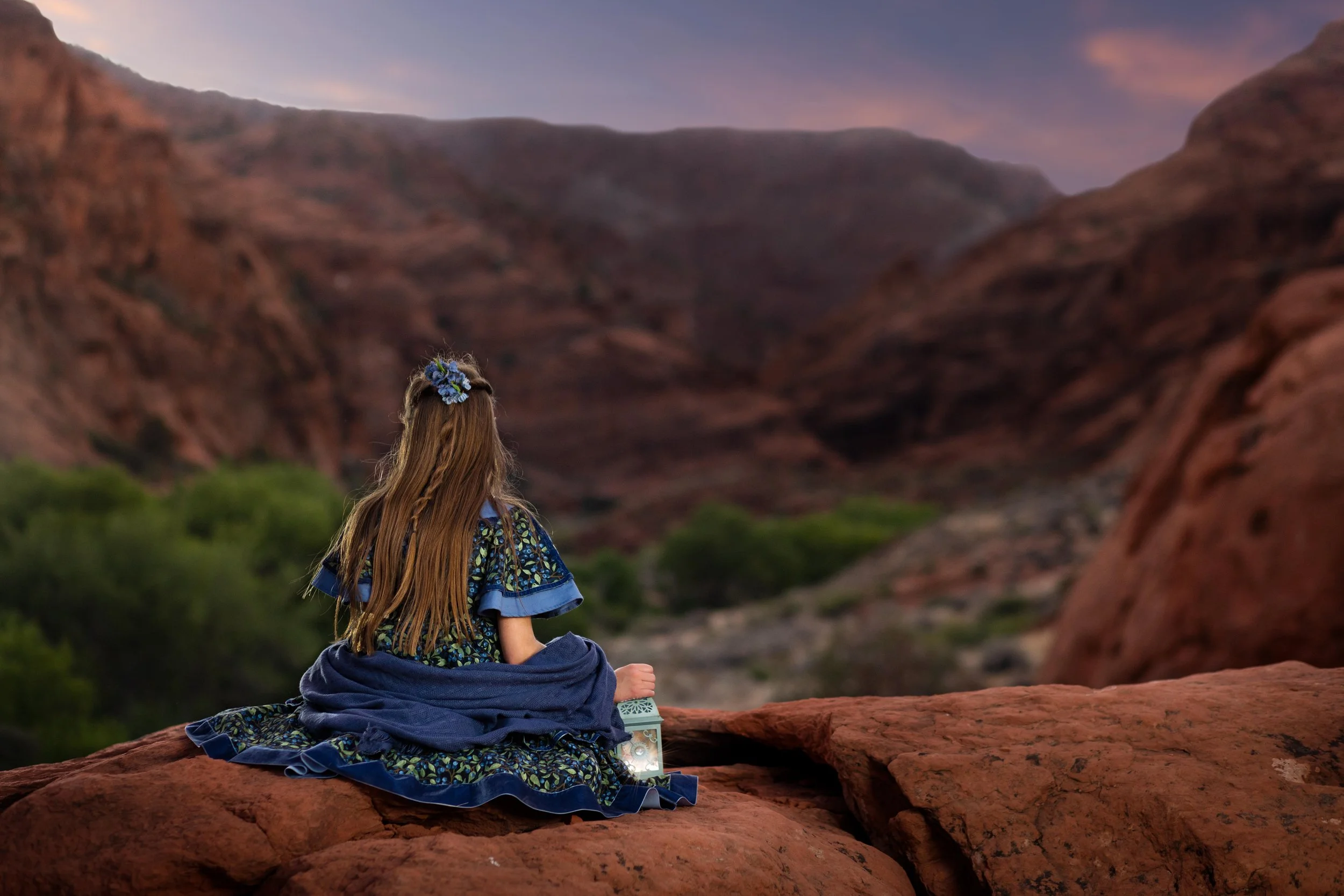 Girl in floral dress with lantern overlooking red rock canyon at dusk, southern Utah