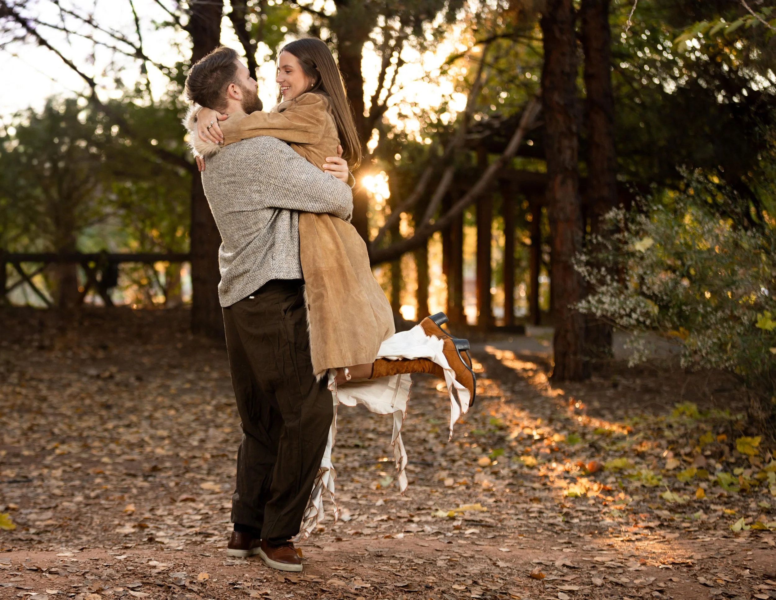Man picks up and twirls women around in soft evening light of autumn during cinematic engagement session in Saint George Utah.
