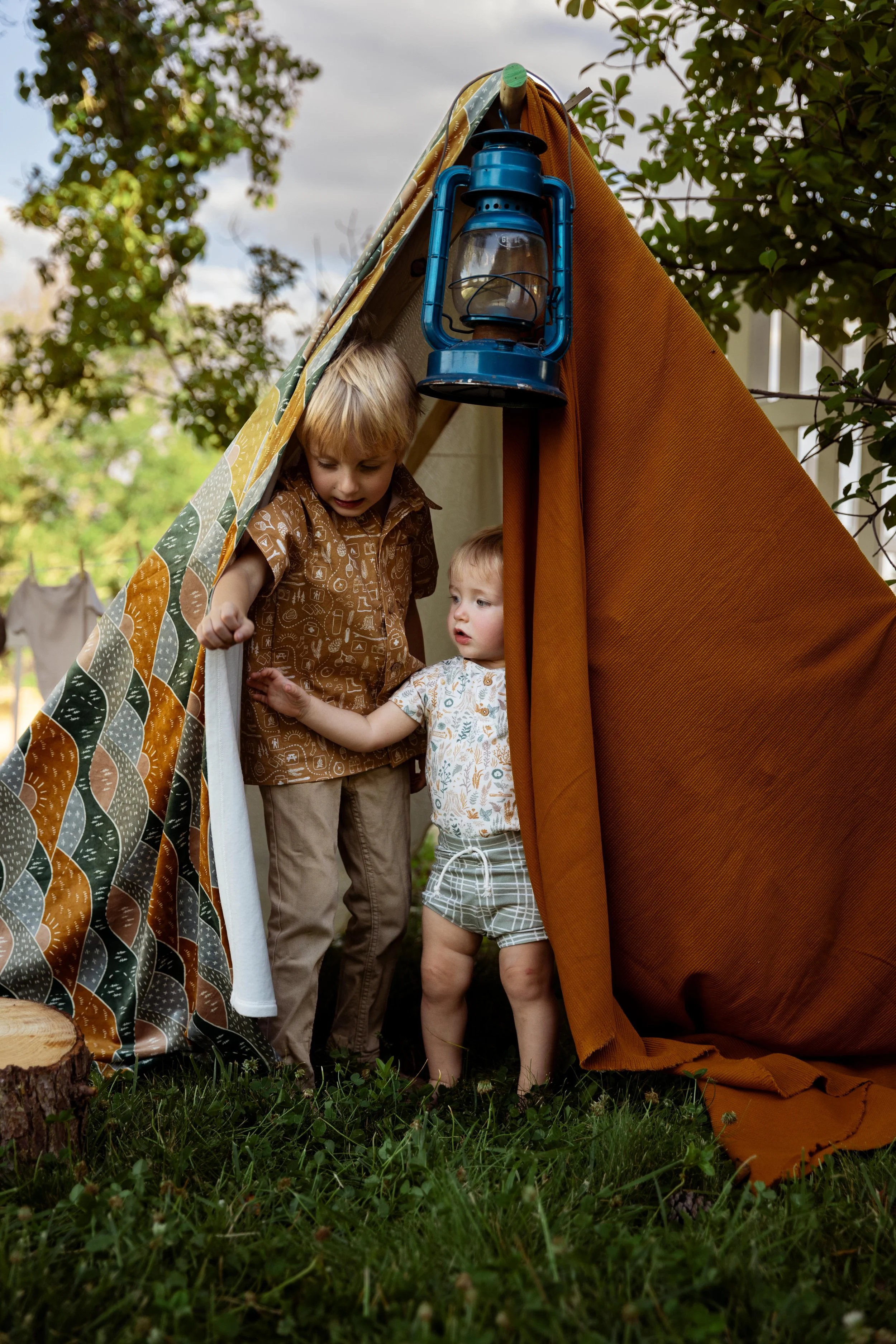 Two children peeking out of a blanket fort tent imagining they are camping in saint George ut during their portrait session in southern utah.