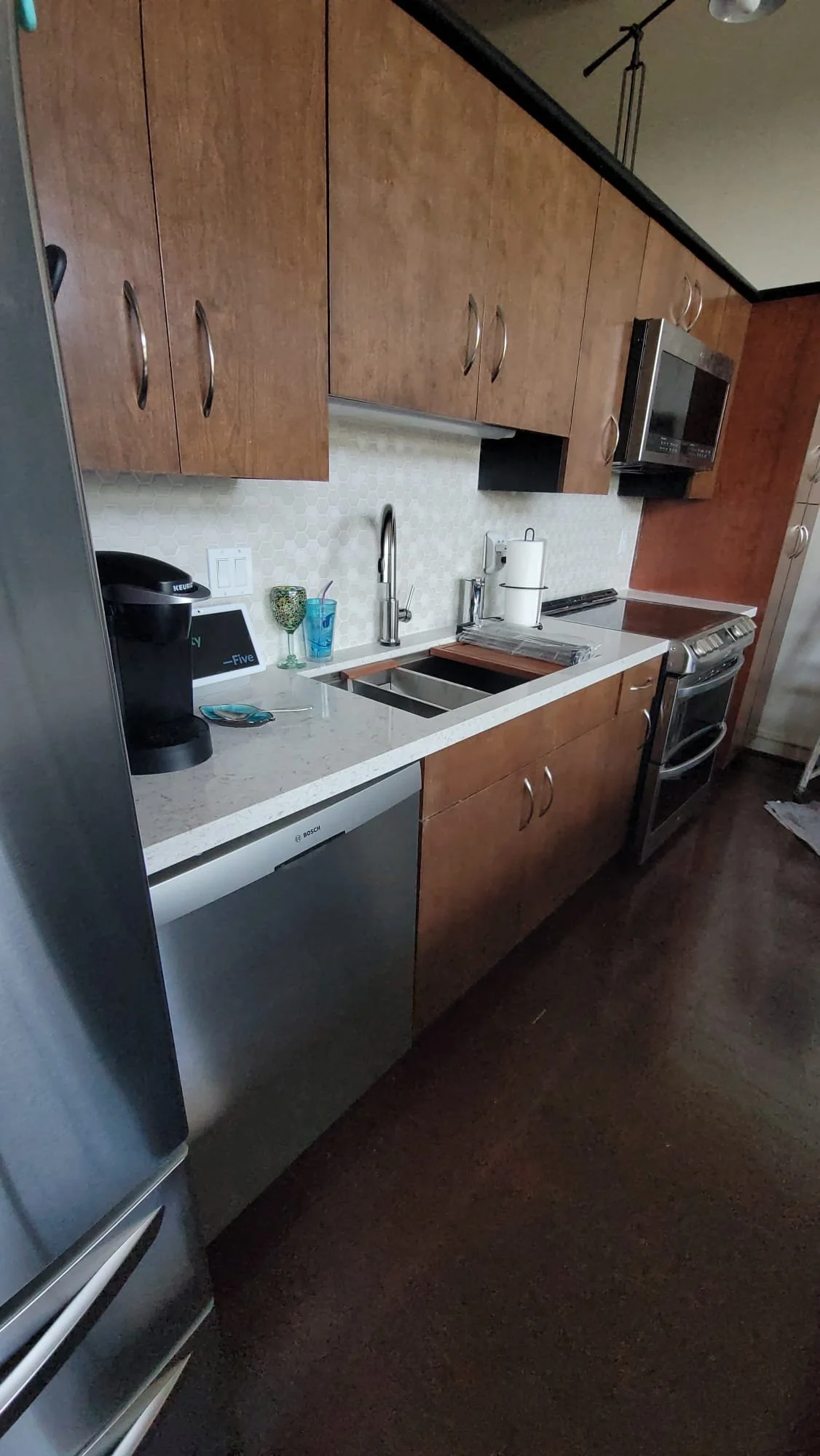 Modern kitchen with wooden cabinets, stainless steel appliances, and marble countertops. Features include a Keurig coffee maker, a microwave, a dishwasher, a dual sink, and a gas stove.