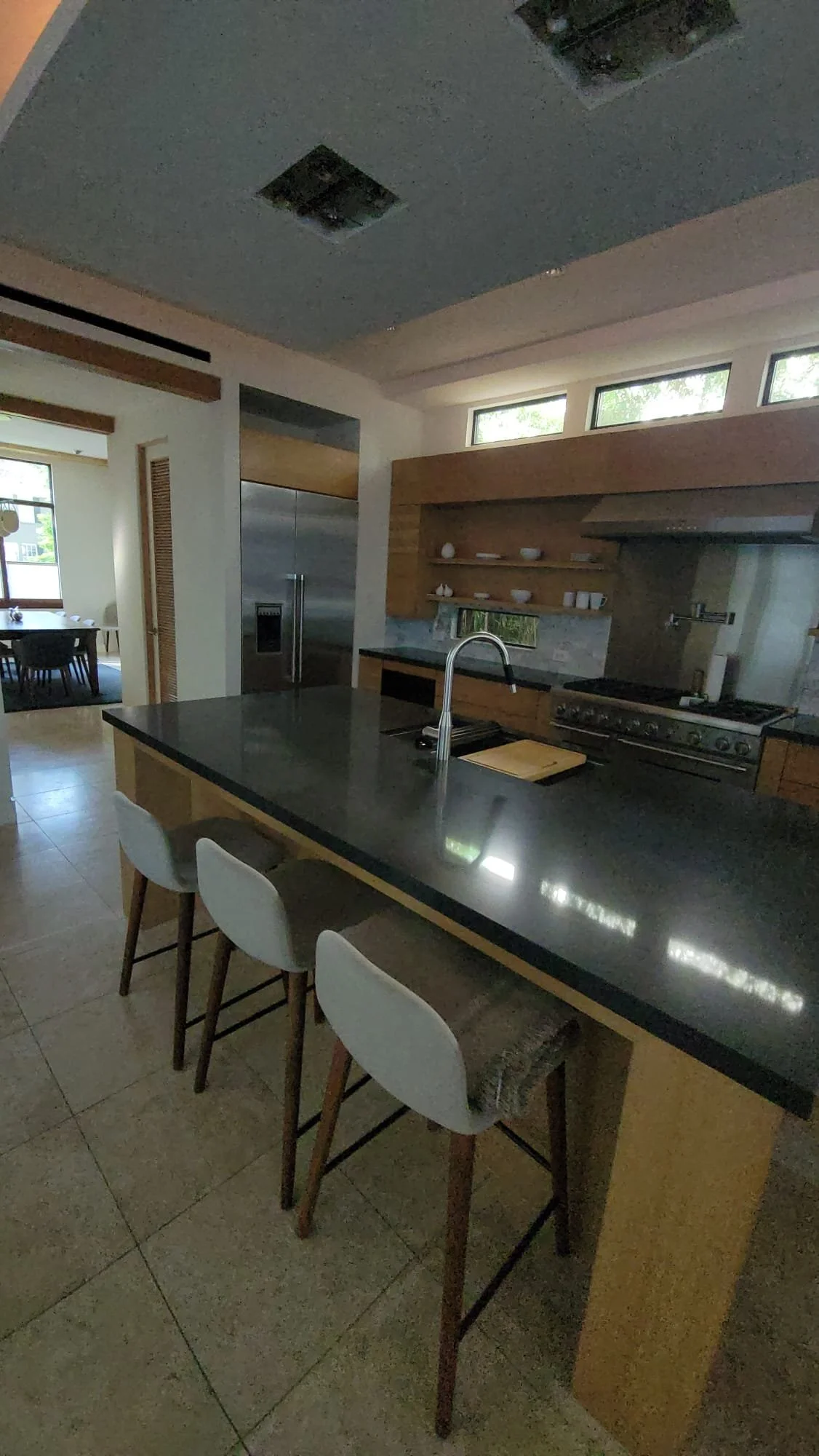 Modern kitchen with a large island, bar stools, stainless steel appliances, and open shelves.