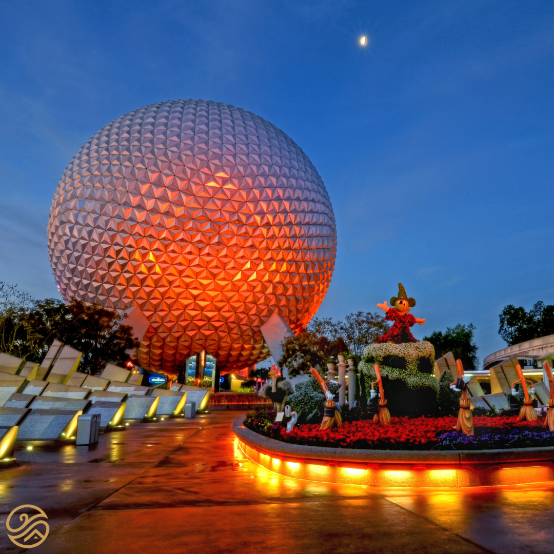 The Globe at Epcot is illuminated bright red. Theres a crescent moon in the sky. A Mickey Mouse statue can be seen close to the Epcot Globe.