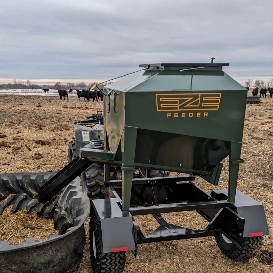 A UTV15 Eze-Feeder portable livestock feeder on a trailer in a muddy field feeding cattle