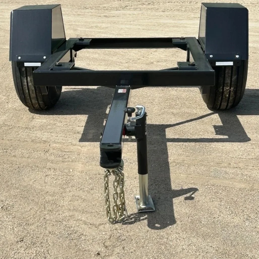 An empty black trailer, made for hauling small grain bins  sitting on a dry gravel lot