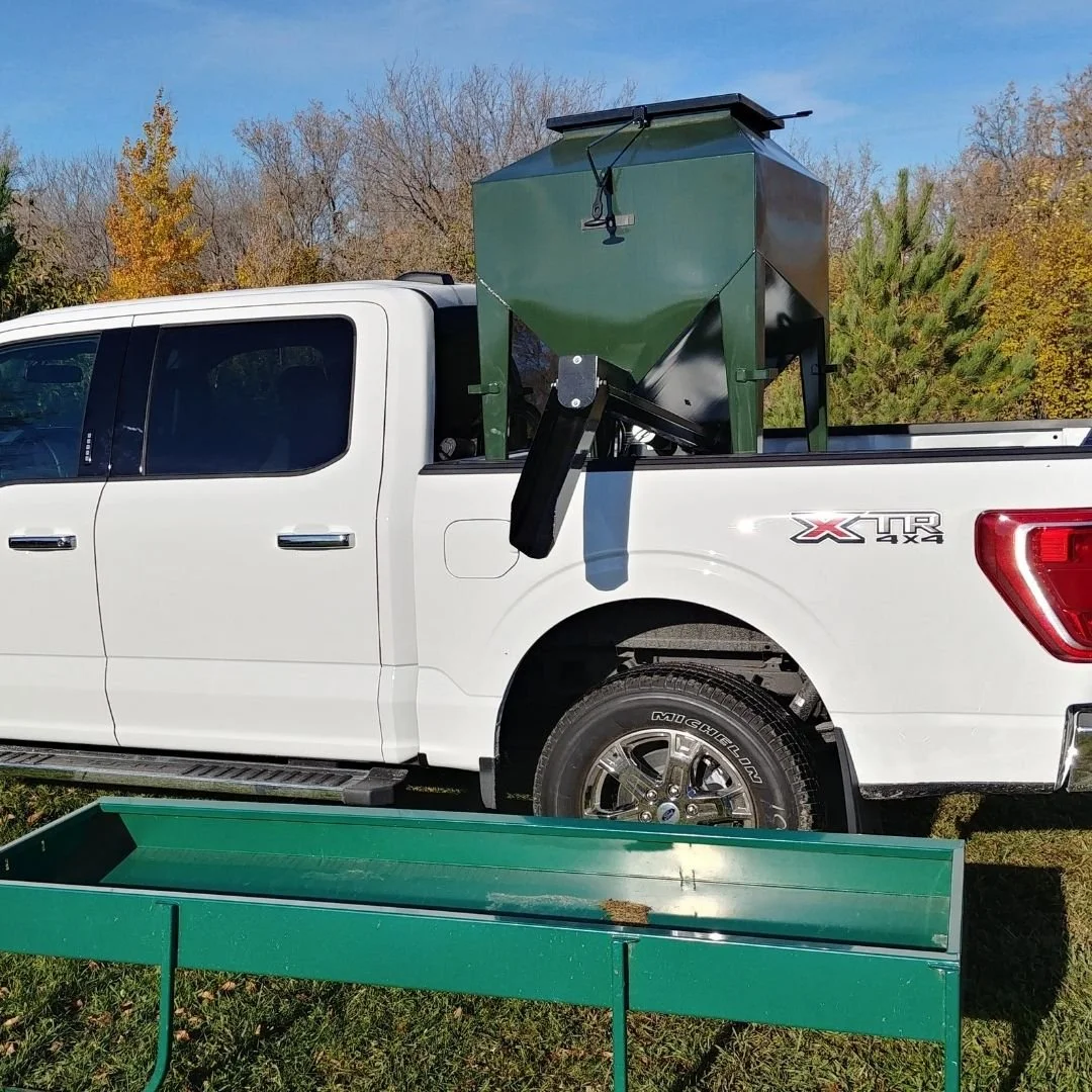 A green livestock feeder with a black spout in the back of a white ford pick up