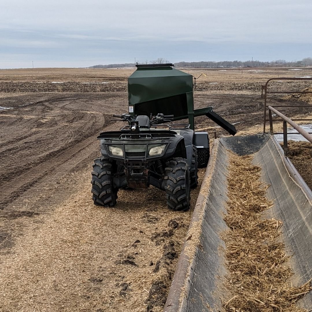 Eze-Feeder UTV15 being pulled by a quad in a  muddy farm field.