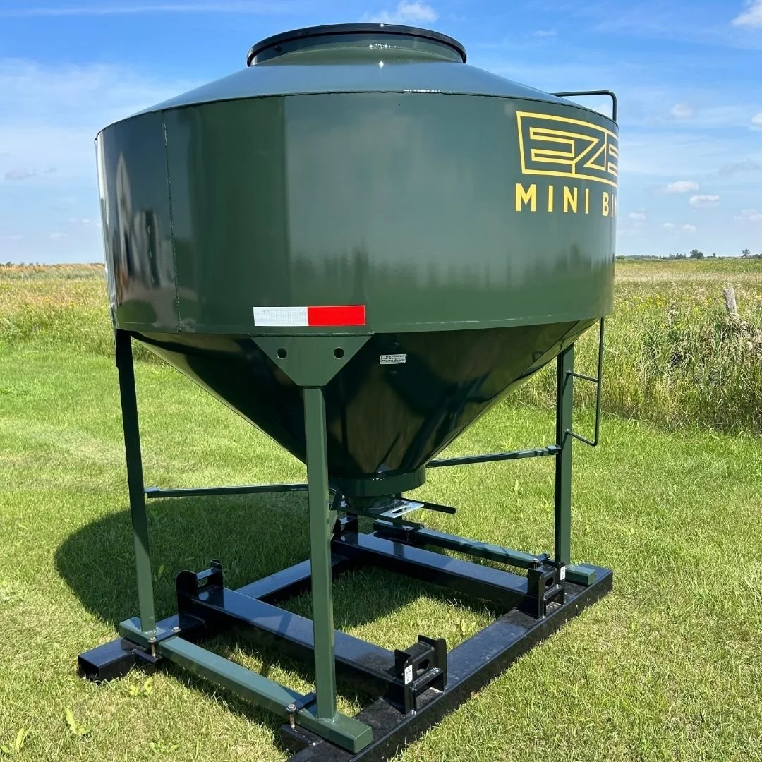 Side view of a green feed storage bin with EZE Mini Bin logo in a rural field with blue skies