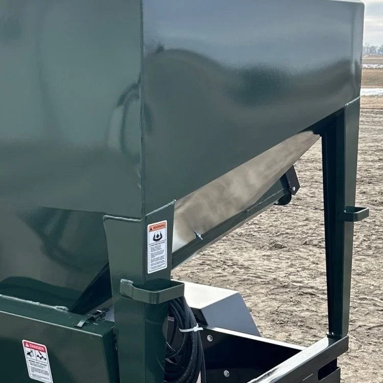 Close-up of built in tie down brackets on the UTV Feeder on a dirt surface, with safety warning labels and cables.