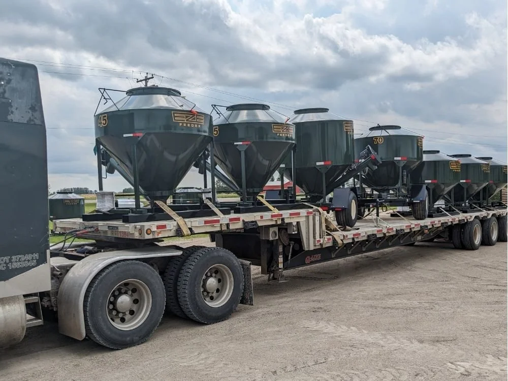 A flat deck truck loaded with various sizes of EZE-Feeder cattle grain feeders.