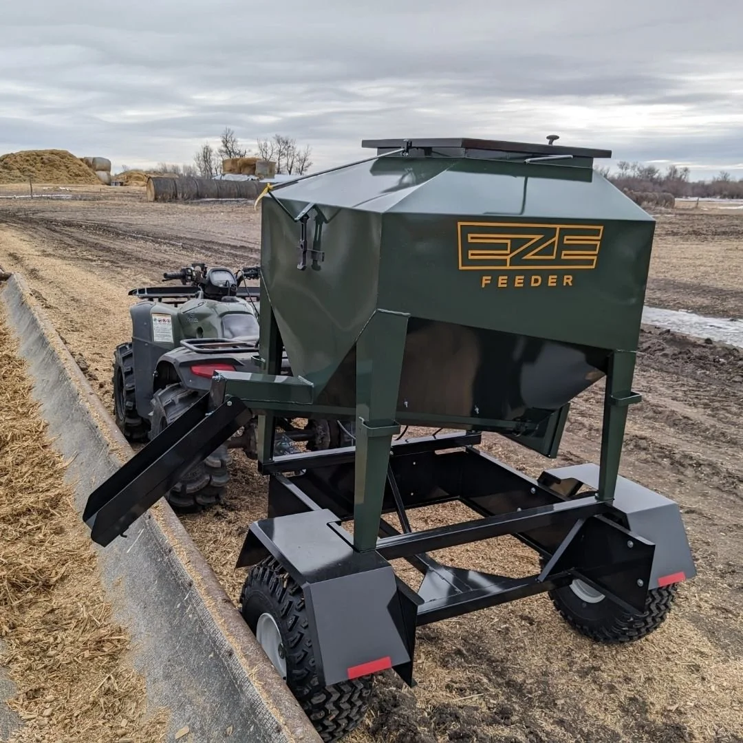 UTV15 eze-feeder hooked up to a grey quad, in a muddy farm field, filling bunk feeders.