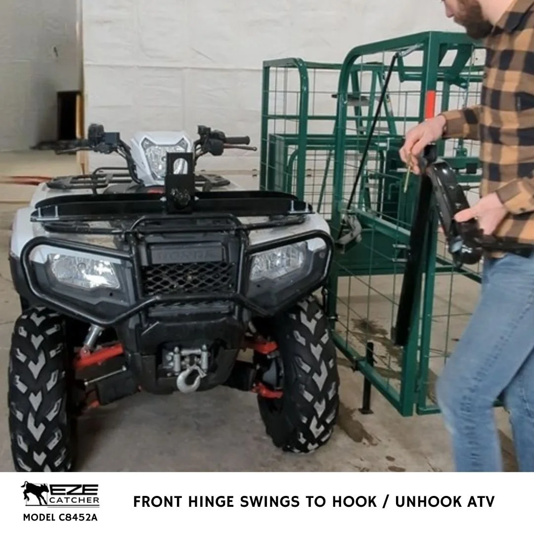 An ATV in a shop being attached to an eze-catcher calf catcher with a front mount hitch by a man in a brown shirt