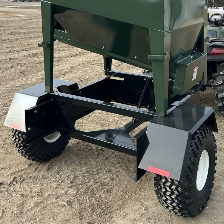 A close up of the back of a green UTV15 EZE-Feeder ATV Feeder Trailer with knobby ATV tires on a dirt surface, 