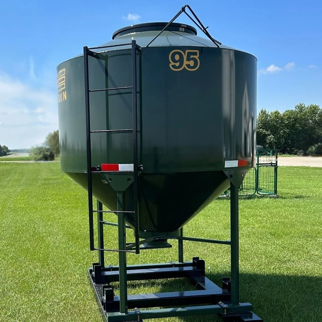 A green grain storage tank, 95 bushel EZE Mini-Bin  sitting on lush green grass with trees in the background