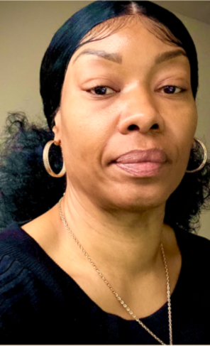 Close-up of a woman with dark hair, hoop earrings, and a necklace, wearing a black top.